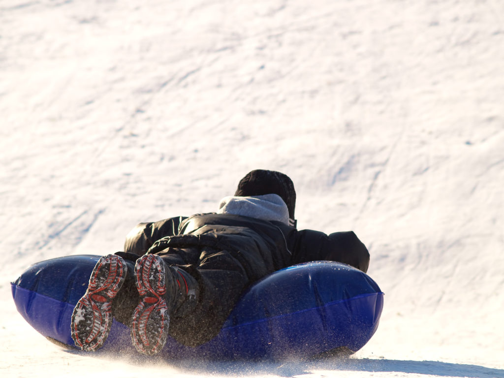 boy sledding down a snowy hill on a blue inflatable sled