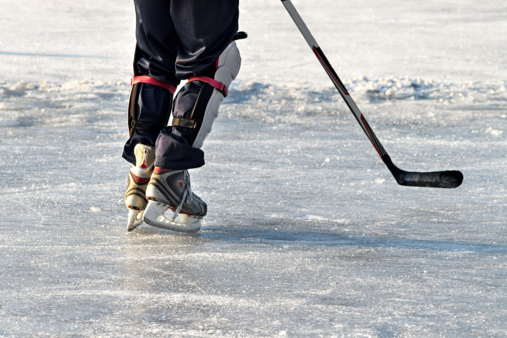 Close-up of skates on player feet during ice hockey. Hockey player practising on a frozen pond outdoor. People playing amateur hockey. Winter playing, fun, snow.