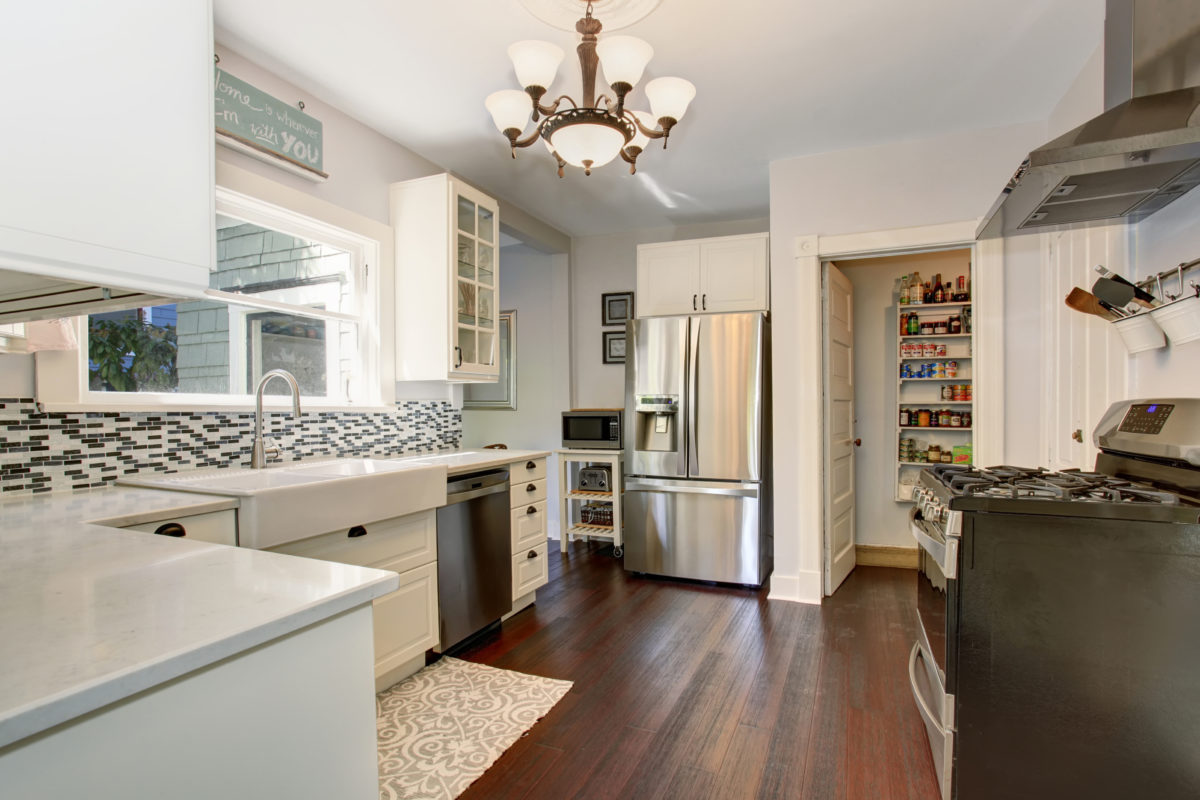 White kitchen room with stainless steel fridge and hardwood floor. View of a pantry.