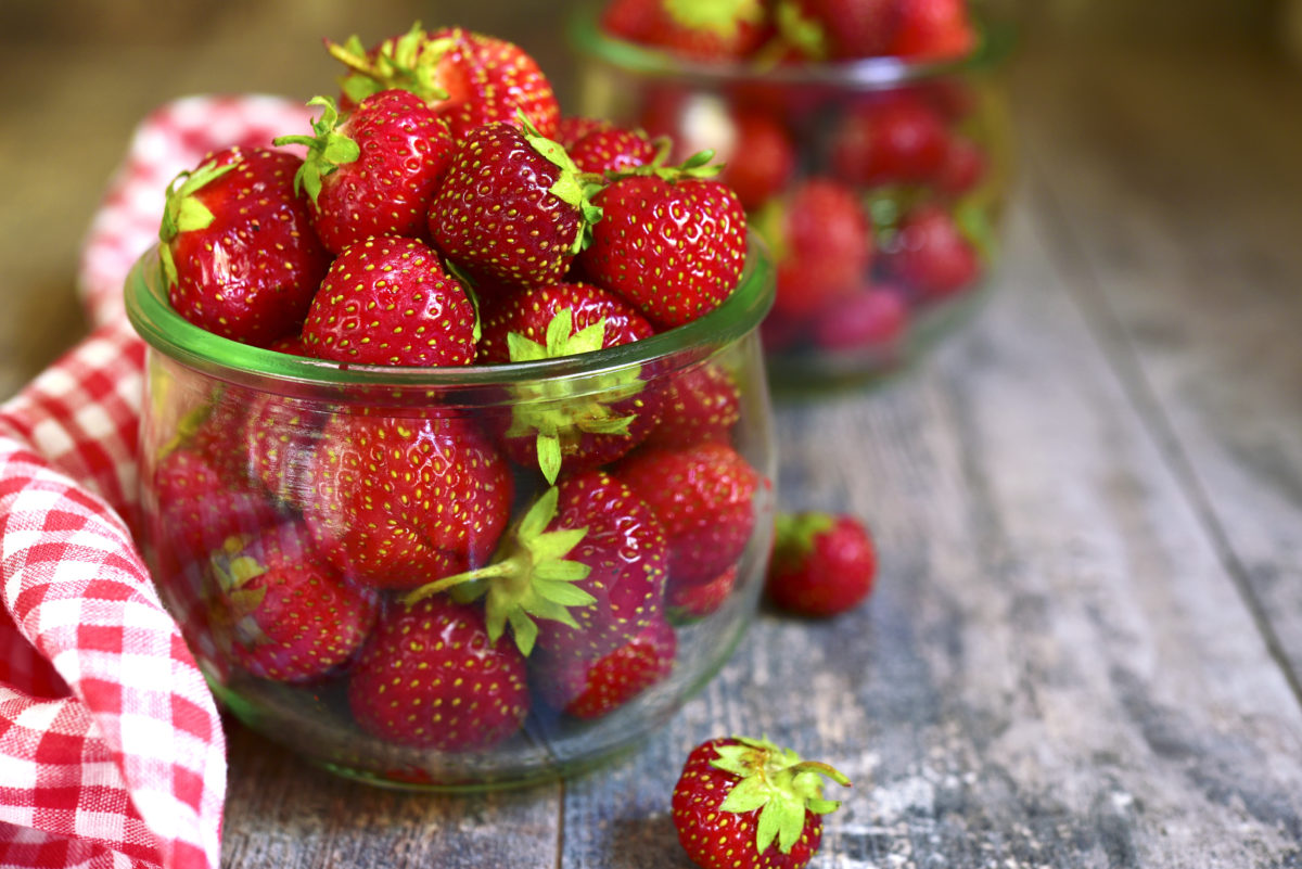 Organic ripe strawbery in a vintage glass jar on a wooden background.