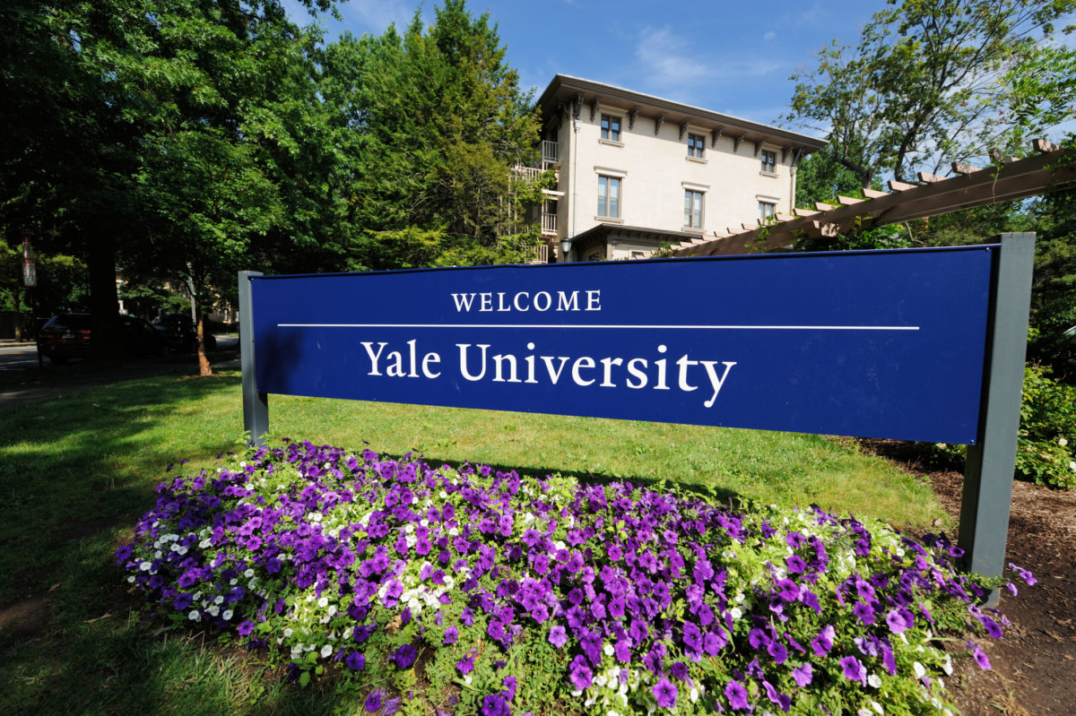 New Haven, Connecticut, USA - July 25, 2016: Welcome to Yale University sign located along Trumbull Street in New Haven, Connecticut. Photograph taken with purple flowers blooming in the foreground